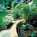 Garden hose with spray nozzle near a garden bed with flowers and plants.